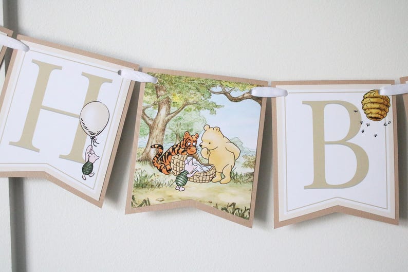 May include: A Winnie the Pooh themed banner with the letters "H" and "B" in a cream color with brown trim. The "H" features a small illustration of Piglet holding a balloon. The "B" features a beehive with bees flying around it. The middle section of the banner features a scene with Winnie the Pooh, Tigger, and Piglet.