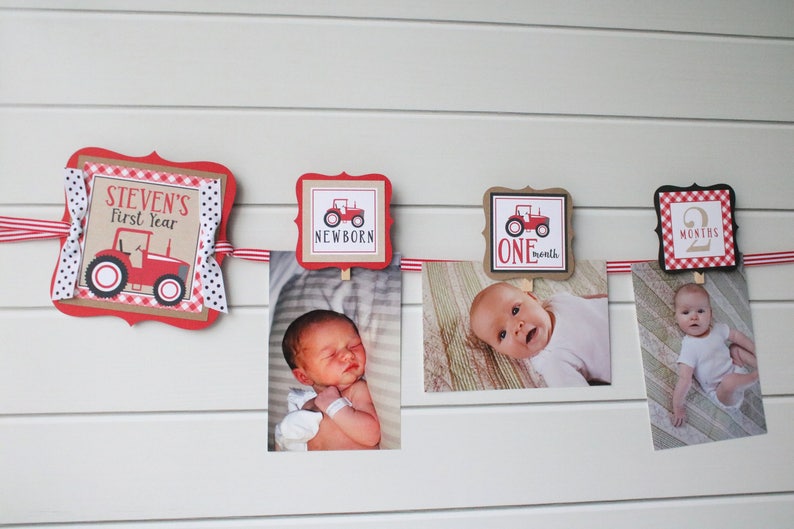 May include: A red and white baby milestone banner with a red tractor design. The banner includes the text "Steven's First Year", "Newborn", "One Month", and "2 Months". The banner is decorated with red and white gingham and black and white polka dots. There are photos of a baby at different ages attached to the banner.