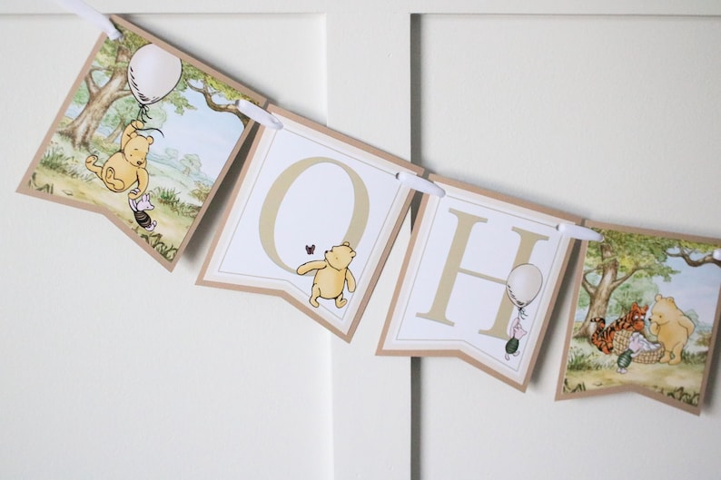 May include: A Winnie the Pooh themed banner with the letters "OH" and a Winnie the Pooh illustration on each end. The banner is made of brown cardstock with white letters and illustrations.