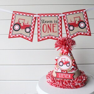 May include: Red and white checkered banner with a red tractor graphic and the text "Steven is ONE". A red and white checkered party hat with a red tractor graphic and the text "Steven" on a brown banner.