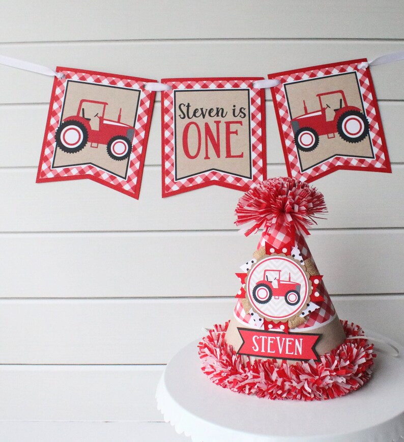 May include: Red and white checkered banner with a red tractor graphic and the text "Steven is ONE". A red and white checkered party hat with a red tractor graphic and the text "Steven" on a brown banner.