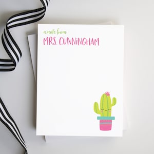 May include: A white card with green text that says "a note from MRS. CUNNINGHAM". A green cactus with a pink flower and a blue pot is in the bottom right corner of the card.