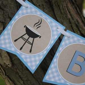 May include: A blue and white gingham banner with a brown circle containing a black grill with smoke coming out of it and a blue circle containing the letter B.