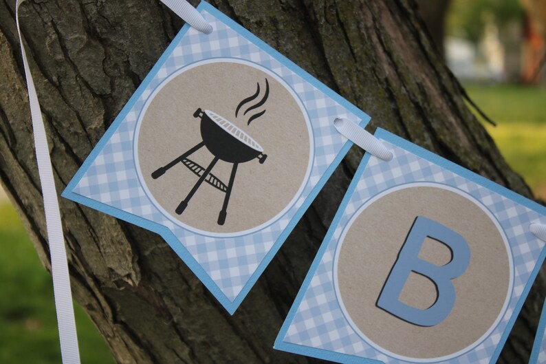 May include: A blue and white gingham banner with a brown circle containing a black grill with smoke coming out of it and a blue circle containing the letter B.