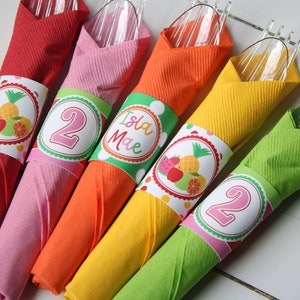 May include: Five colorful paper napkin rings with fruit designs and the number "2" and the name "Isla Mae" printed on them. The rings are wrapped around clear plastic forks.