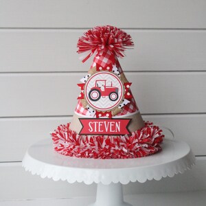 May include: Red and white checkered birthday party hat with a red tractor graphic and the name "STEVEN" on a banner.