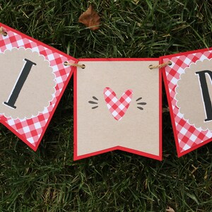 May include: Red and white gingham banner with the words "I love D" in black letters. The banner is strung with twine and has a heart-shaped design in the middle.