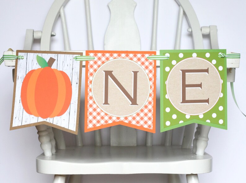 Puede incluir: Una pancarta de tem&aacute;tica oto&ntilde;al con una calabaza, cuadros vichy y lunares. La pancarta dice "ONE" en letras marrones.