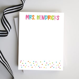 May include: White notepad with the text "MRS. HENDRICKS" in colorful letters at the top. The bottom of the notepad has a border of colorful confetti.