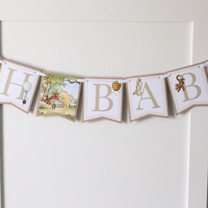 May include: A Winnie the Pooh themed baby shower banner with the letters "OH BABY" in gold lettering on a white background. Each letter is decorated with a Winnie the Pooh character.