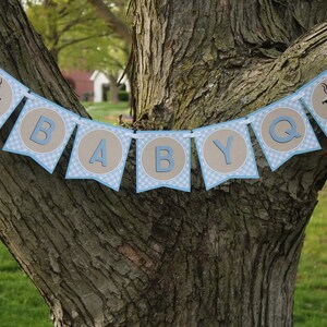 May include: A blue and brown banner with the words "BABY Q" and a grill icon on each end. The banner is hanging from a tree branch.