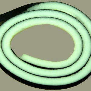 Op de afbeelding: Een opgerolde rol zwarte en witte schuimrubberen weerdichting. Het schuim is lichtgroen van kleur en heeft een zwarte buitenlaag.