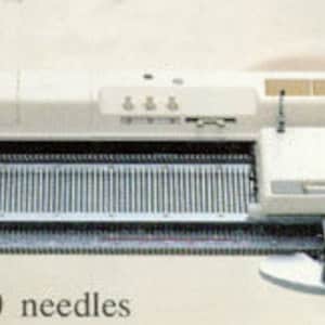 May include: A white knitting machine with 200 needles and a needle pitch of 4.5 mm. The machine has a handle on the left side and a control panel on the right side.