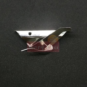May include: A shiny, silver-colored metal clip, possibly for holding fabric or paper. The clip has a triangular base with a curved, angled top and a small hole. The background is a dark, textured surface.
