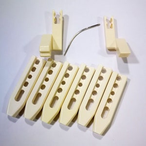 May include: A set of eight off-white plastic knitting needles with a metal needle for joining the needles. The needles have a U-shaped design with holes along the sides.