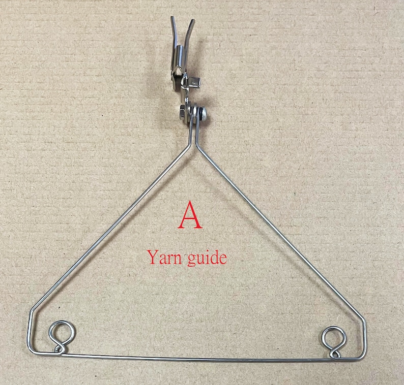 May include: A silver metal yarn guide with two loops at the bottom and a hook at the top. The yarn guide is shaped like a triangle. The text "A Yarn guide" is written below the triangle.