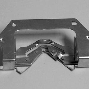 May include: A silver metal bracket with a series of interlocking metal pieces. The bracket has a rectangular shape with a cut-out in the center.