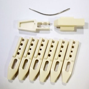 May include: A set of seven off-white plastic knitting needles with a metal needle for threading yarn. The needles have a pointed tip and a rounded base.