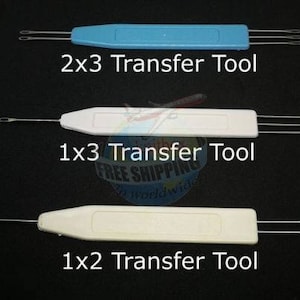Puede incluir: Tres herramientas de transferencia de gancho de ganchillo con diferentes configuraciones de agujas. Las herramientas son de plástico blanco y azul con agujas de metal. Las herramientas están etiquetadas como "2x3 Transfer Tool", "1x3 Transfer Tool" y "1x2 Transfer Tool".