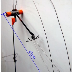 Puede incluir: Un comedero para pájaros de alambre plateado con una base de metal negro y piezas de plástico naranja. El comedero mide 41 cm de alto.
