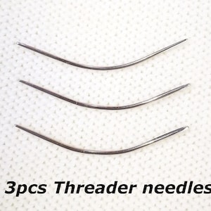 May include: Three silver needle threaders, curved in shape, are arranged in a row on a white textured surface. The text "3pcs Threader needles" is printed below the needles.