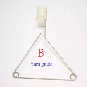 May include: A white plastic yarn guide with a metal triangle yarn guide with the letter "B" and the text "Yarn guide" printed on it.
