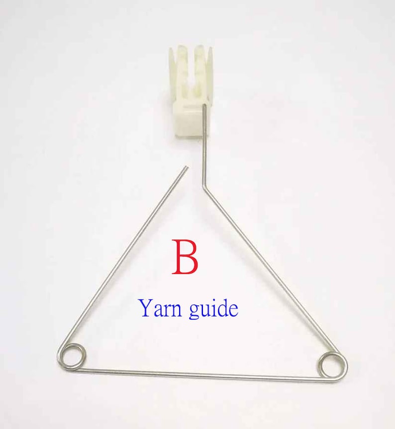 May include: A white plastic yarn guide with a metal triangle yarn guide with the letter "B" and the text "Yarn guide" printed on it.
