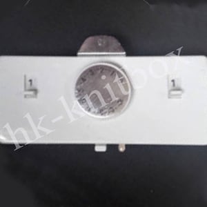 May include: White plastic sewing machine accessory with a round dial that has numbers 1 through 5. The dial has a silver metal cover. There are two buttons on the accessory, each labeled with the number 1.