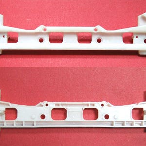 Puede incluir: Dos piezas de coche de plástico blanco idénticas con múltiples agujeros y ranuras. Las piezas se muestran desde arriba y abajo.