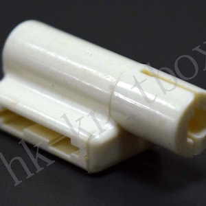 May include: A white plastic connector with a slot and a round opening. The connector is designed for electrical wiring.