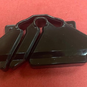 May include: A black plastic hanger accessory with a unique design. The accessory has a rectangular base with two triangular sections and a curved top section. The object is on a red surface.