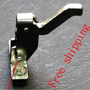 Könnte beinhalten: Ein silberner Metallhebel mit einem Griff, der in einem 90-Grad-Winkel gebogen ist. Der Hebel ist mit einer Schraube an einer Metallbasis befestigt. Der Hebel dient zum Öffnen und Schließen einer Tür oder eines Fensters.