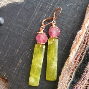 May include: A pair of dangle earrings with a copper wire design. Each earring features a pink glass bead and a long, rectangular green stone.