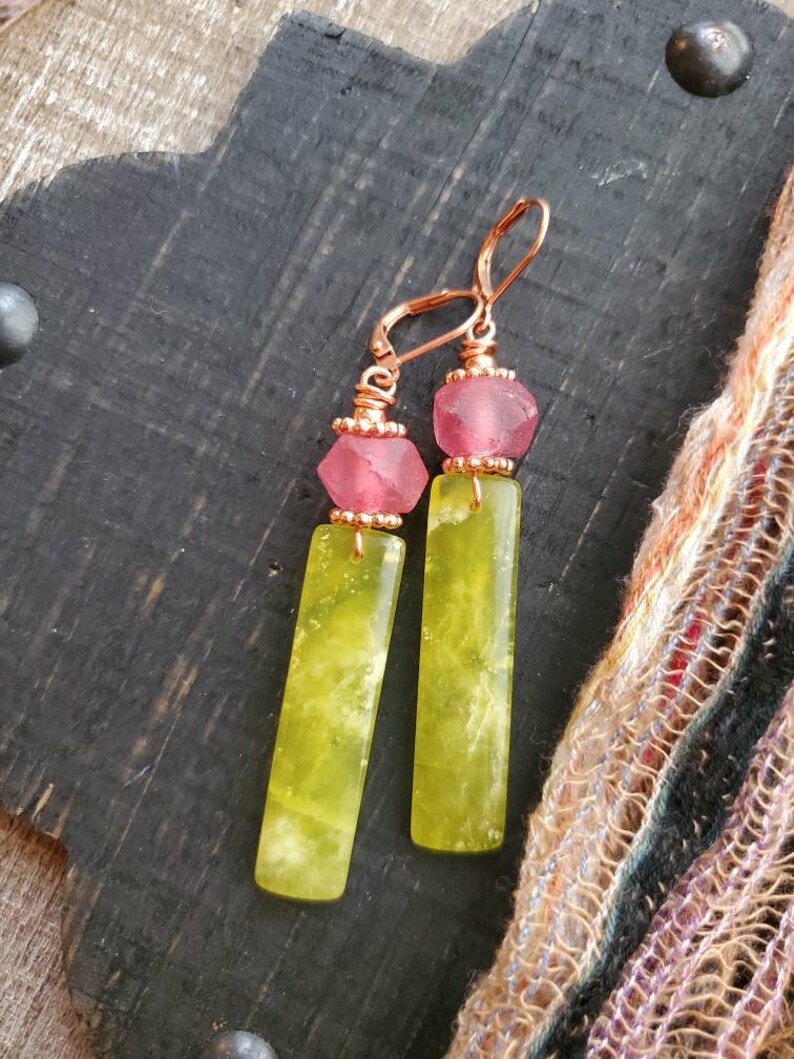 May include: A pair of dangle earrings with a copper wire design. Each earring features a pink glass bead and a long, rectangular green stone.