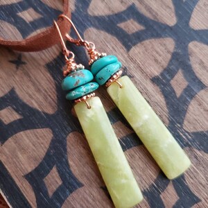May include: A pair of dangle earrings with green jade stone and turquoise beads. The earrings are made with copper wire and have a simple design.