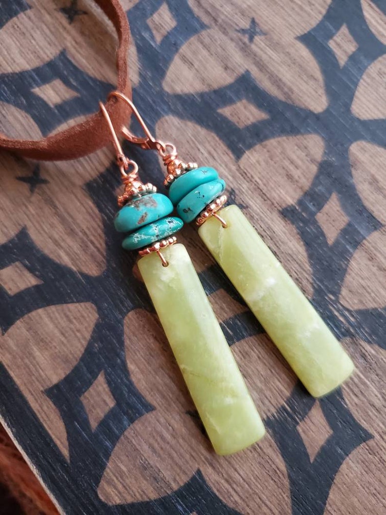 May include: A pair of dangle earrings with green jade stone and turquoise beads. The earrings are made with copper wire and have a simple design.