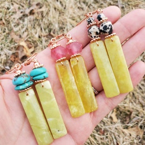 May include: Three pairs of dangle earrings with different colored stones and beads. The earrings feature a long, rectangular, light green stone with gold-toned metal accents.