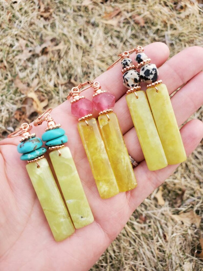 May include: Three pairs of dangle earrings with different colored stones and beads. The earrings feature a long, rectangular, light green stone with gold-toned metal accents.