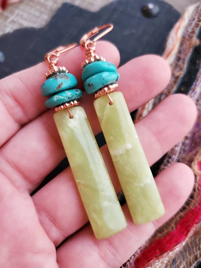 May include: A pair of dangle earrings with green jade stone and turquoise beads. The earrings have a copper wire design.