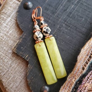 May include: A pair of dangle earrings with a green stone and black and white dalmatian jasper beads. The earrings have copper wire accents.
