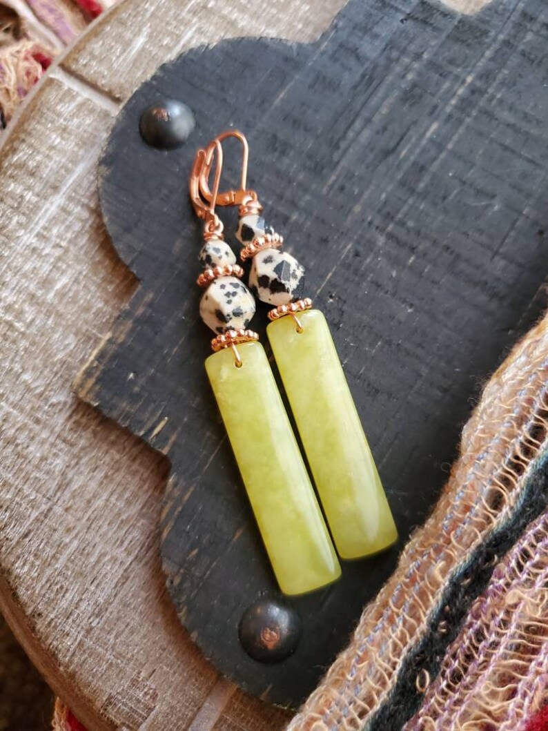 May include: A pair of dangle earrings with a green stone and black and white dalmatian jasper beads. The earrings have copper wire accents.