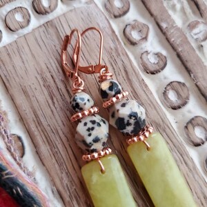 May include: A pair of dangle earrings with a copper wire wrapped around a light green stone and a black and white dalmatian jasper stone. The earrings have a copper hook.