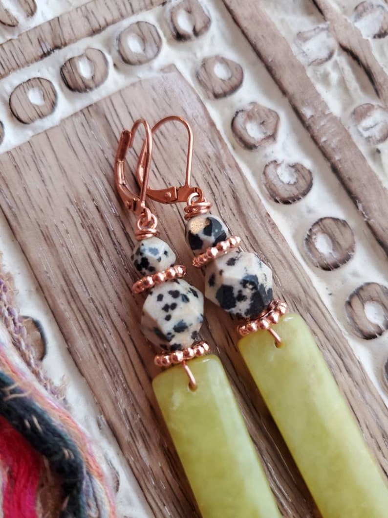 May include: A pair of dangle earrings with a copper wire wrapped around a light green stone and a black and white dalmatian jasper stone. The earrings have a copper hook.