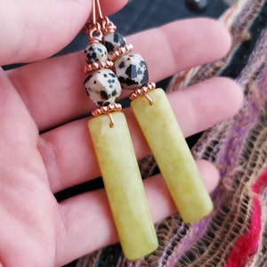 May include: A pair of dangle earrings with a copper wire design. The earrings feature a green jade stone and a black and white dalmatian jasper stone.