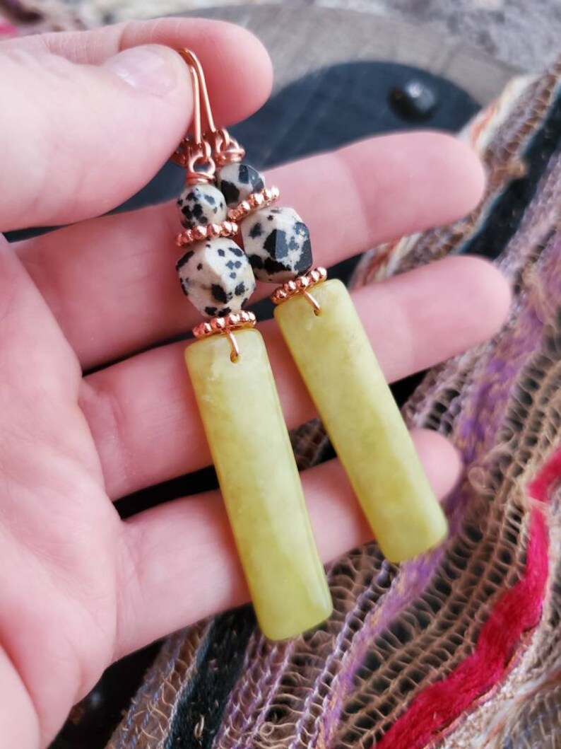 May include: A pair of dangle earrings with a copper wire design. The earrings feature a green jade stone and a black and white dalmatian jasper stone.