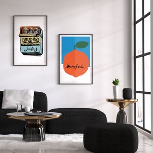 May include: Two framed prints on a white wall. The print on the left is a yellow and blue illustration of a sardine can. The print on the right is a blue and orange illustration of a mandarin orange with the word "Mandarin" written in black.