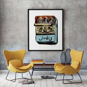 May include: A framed illustration of a blue and white sardine can with three sardines inside. The can has the word "Sardines" written on it in black lettering. The illustration is on a white background.