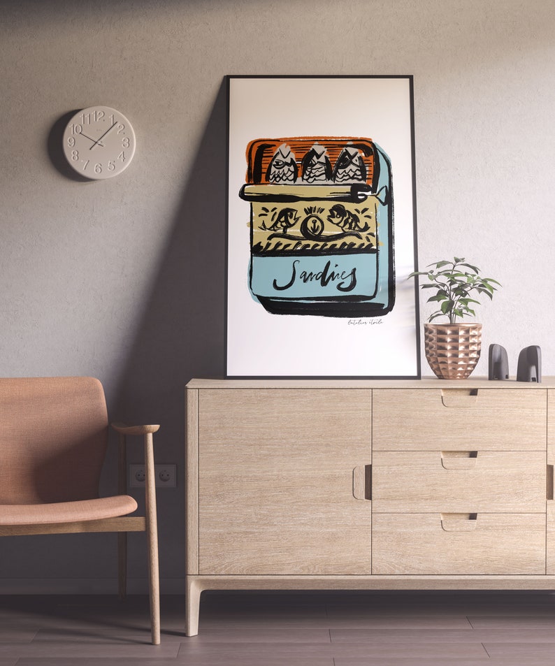 May include: A framed illustration of a blue and yellow can of sardines with three fish inside. The can has the word "Sardines" written on it in black cursive. The illustration is on a white background.