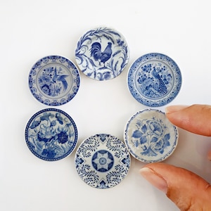 Peut inclure: Six assiettes en porcelaine bleue et blanche avec différents motifs floraux et animaliers. Les assiettes sont disposées en cercle sur un fond blanc.