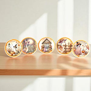 Puede incluir: Cinco posavasos redondos con bordes naranjas, cada uno con una ilustración temática de Halloween. Los diseños incluyen gansos con sombreros de bruja, calabazas y una escena de granero espeluznante. Los posavasos están colocados sobre una superficie de madera.